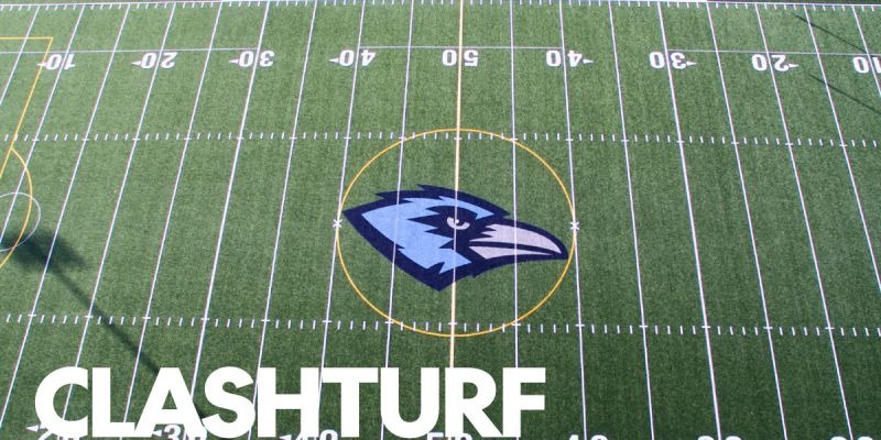 Aerial view of a turf football field with yard lines and midfield logo
